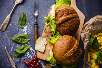Fast food on the table: burger with beef or pork, or chicken and vegetables, French fries with tomato sauce, basil leaves