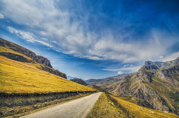 Straight empty highway leading into Xinalig village. Beautiful landscape of big Caucasus mountains and road country road with blue cloudy sky and yellow grass. Azerbaijan Guba nature