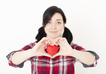 Smiling young girl holding a small red heart and her fingers in 
