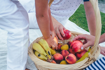 Family picnic. A lot of hands in a basket with fruits: bananas, oranges, nectarines, apricots 