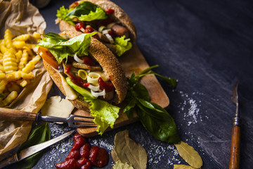 Fast food on the table: hot dog sausage and vegetables, French fries with tomato sauce, basil leaves