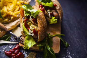 Fast food on the table: hot dog sausage and vegetables, French fries with tomato sauce, basil leaves