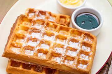 Whole wheat Belgium waffles on plate with butter, maple sauce on wooden table