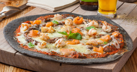 Black pizza with seafood: shrimps, salmon, mussels.