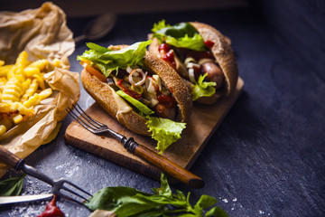 Fast food on the table: hot dog sausage and vegetables, French fries with tomato sauce, basil leaves