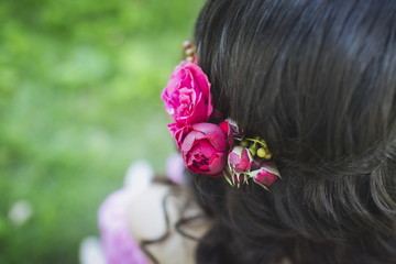 Beautiful peony flowers in hair of a happy bride on sunny summer wedding day. Long black curly hair, wedding hairstyle, close up. Copy space, blurred background