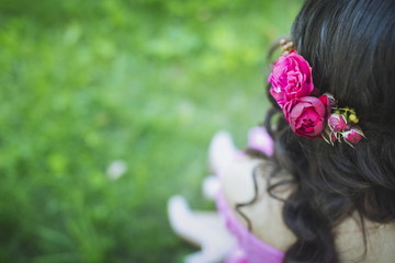 Beautiful peony flowers in hair of a happy bride on sunny summer wedding day. Long black curly hair, wedding hairstyle, close up. Copy space, blurred background