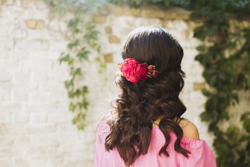 Beautiful peony flowers in hair of a happy bride on sunny summer wedding day. Long black curly hair, wedding hairstyle. Copy space, blurred background. Sun rays, sunshine