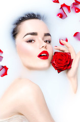 Beauty young model girl with bright makeup and red rose flower relaxing in milk bath