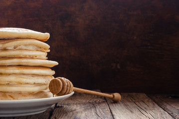 Stack of pancakes with honey on wooden background.