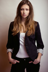 Fashion studio lifestyle portrait of a pretty young brunette model with long hair in black coat.