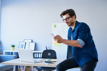 Designer sitting on desk in office using his smartphone