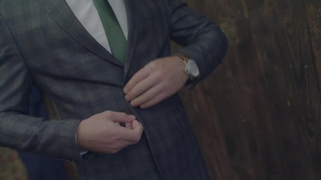 Unrecognizable stylish man dresses buttoning checked jacket and straightening it close up slow motion. Male clothing green tie casual fit expensive wearing vintage retro fashion sewing at tailors 