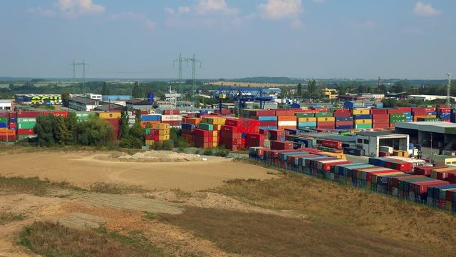 Colorful intermodal containers at a yard, a vast rural area and the blue sky in the background, a spacious area with occasional vegetation in the foreground - top view