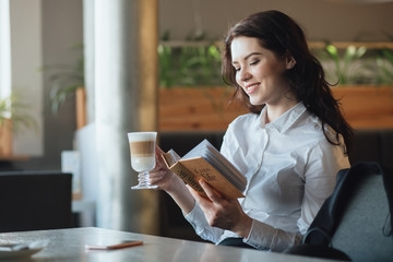 Young woman relaxing in cafe, drinking latte, reading diary book