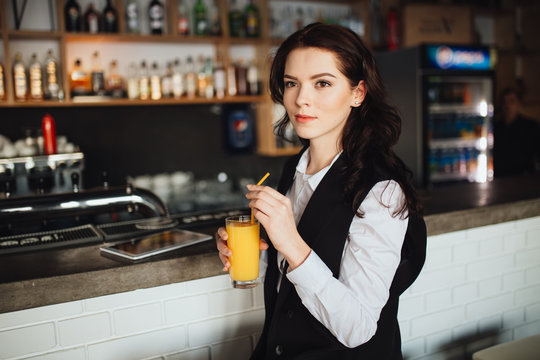 Young woman holding glass of fresh orange juice at restaurant bar. Health trend.