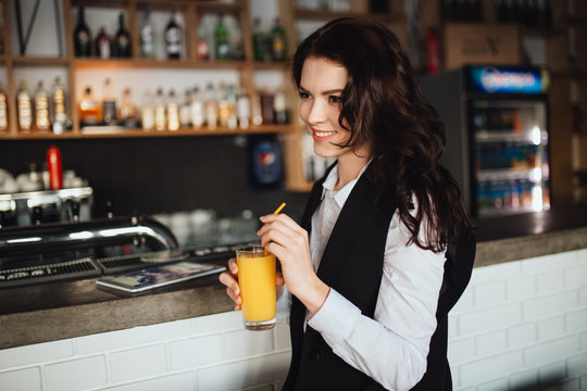 Beautiful woman holding glass of fresh orange juice at restaurant bar. Health trend.