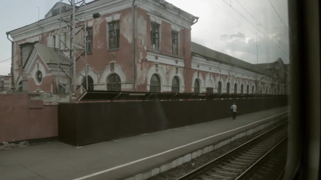 A man walks near the old station. The view from the window of a passenger train.