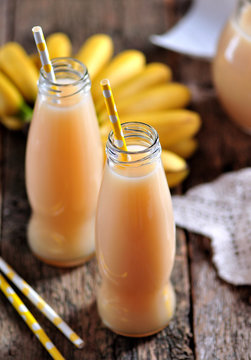 Thick organic banana juice in bottles with straws on an old table.
