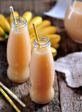 Thick organic banana juice in bottles with straws on an old table.