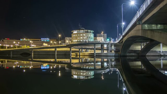 Time Lapse Tilt of urban bridge and waterway at night. Reflections in the water
