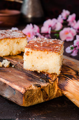 Sweet pie Basbousa or revane or Namoora on wooden plate and dark background with spring flowers. Arabian cuisine. Selective focus