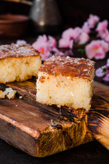 Sweet pie Basbousa or revane or Namoora on wooden plate and dark background with spring flowers. Arabian cuisine. Selective focus