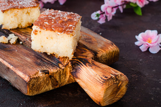 Sweet pie Basbousa or revane or Namoora on wooden plate and dark background with spring flowers. Arabian cuisine. Selective focus