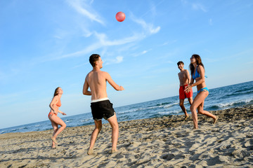 four young people man and woman playing beach volley together by the sea in sunny summer vacation day