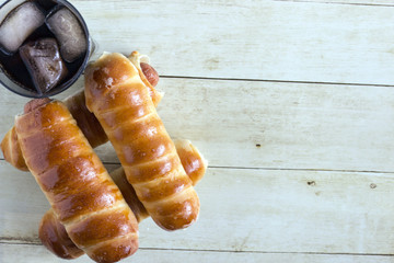 Pigs in a blanket and a glass of sparkling water with ice cubes on light wood background, top view