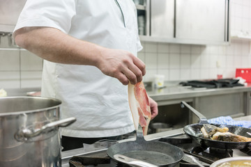 Koch legt Schinken in Pfanne auf dem Herd in einer Hotel oder Restaurant Küche