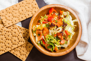 Овощной салат с оливковым маслом в деревянной тарелке и ржаные хлебцы