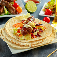 Homemade Kofta kebabs on skewers with pita, lime, vegetables, beer, sweet chili and yogurt sauce on white plate