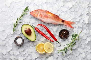 Fresh red mullet fish with lemon, rosemary, avocado, chili pepper and spices on icy stone background