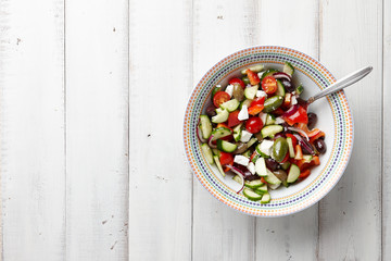 Fresh Greek salad in a big bowl on white wooden background, top view