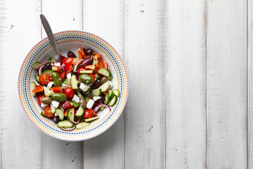 Fresh Greek salad in a big bowl on white wooden background, top view