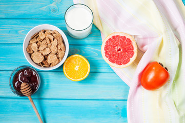 Bowl of healthy corn flakes breakfast cereal, milk and fruits on blue wood table