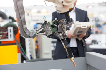Industrial welding robot arm, blurred operator in the background