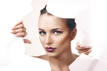 Girl with glamorous makeup looks through the geometric pattern in the paper