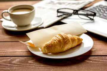 Business lunch with croissant and laptop on wooden desk