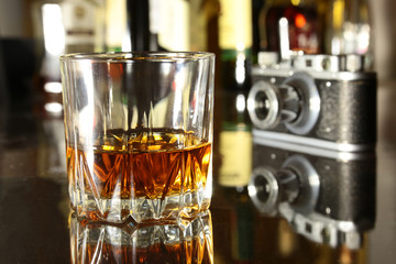 Glass of brandy or cognac and retro camera on the mirror wooden table