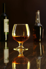 Glass of cognac, brandy or whiscy on black mirror table. bottles in a bar on the background