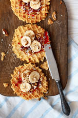 Stack Belgian waffles with walnuts, jam and a banana on a dark wooden background. Sweet food concept.