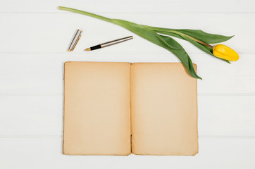 Background with yellow tulips, blank notepad on white wooden table top view. Creative woman's workspace concept with copy space. Product photograph taken from above with frame composition