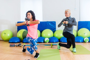 Fit female sportswoman doing curtsy lunge exercise with dumbbells in group fitness studio class