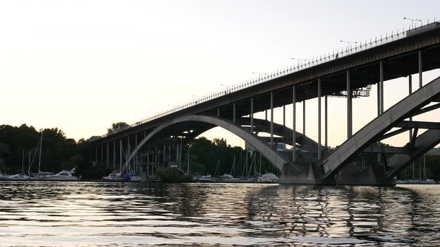 Arch bridge over river at dusk. Marina boats riverside