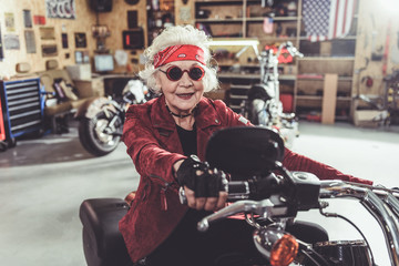 Outgoing grandmother driving motorcycle in mechanic shop