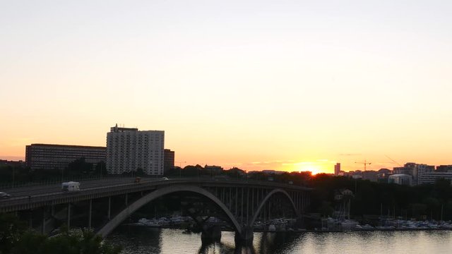 Arch bridge and river at sunset. Traffic passing by, office building in the background