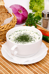 "Okroshka" cold soup with vegetables and chicken in a white bowl decorated parsley, against a background of vegetables