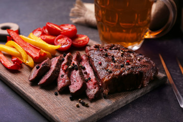 Tasty grilled steak with beer on cutting board